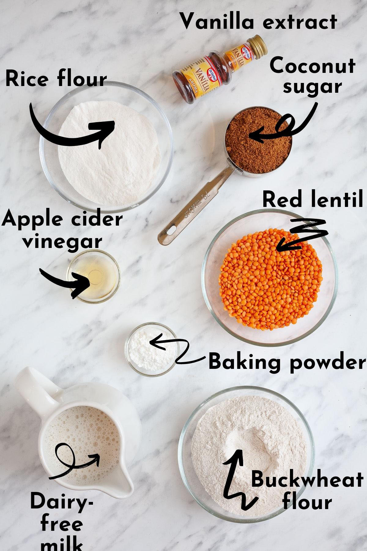 Ingredients for red lentil pancakes measured in glass bowls, white flours, powders, brown coconut sugar, milk in a jar, vanilla extract and of course red lentils