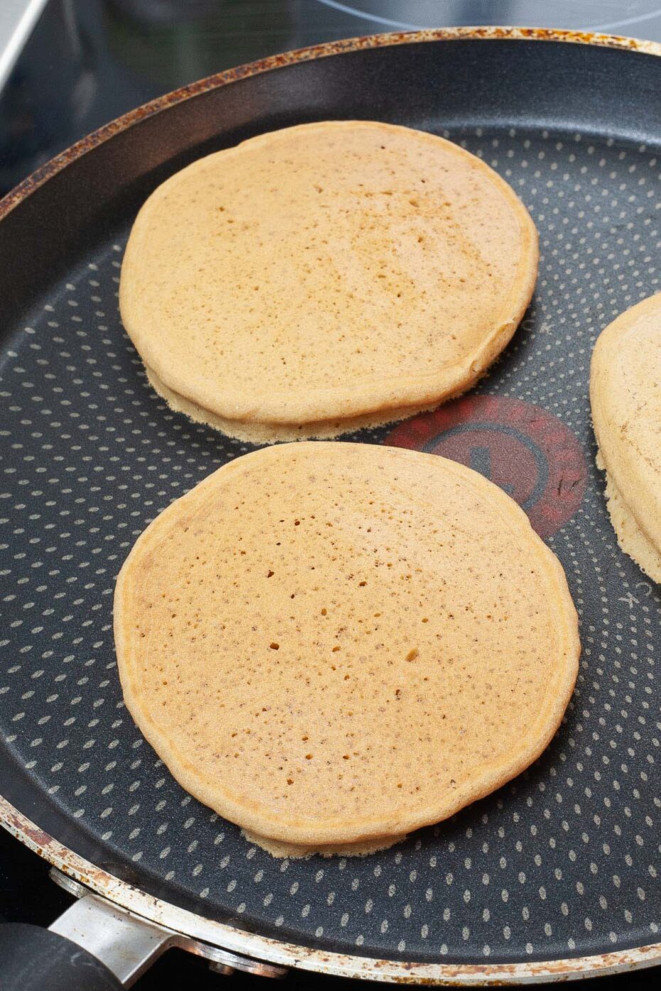 Black frying pan with 3 pancakes with the topped are cooked already