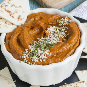 Deep orange brownish cream in a small white bowl topped with green dried herbs and tiny white sees