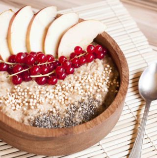 Bowl of Vegan Apple Cinnamon Oatmeal made on stove top - topped with apple slices, red currant, chia seeds and puffed quinoa
