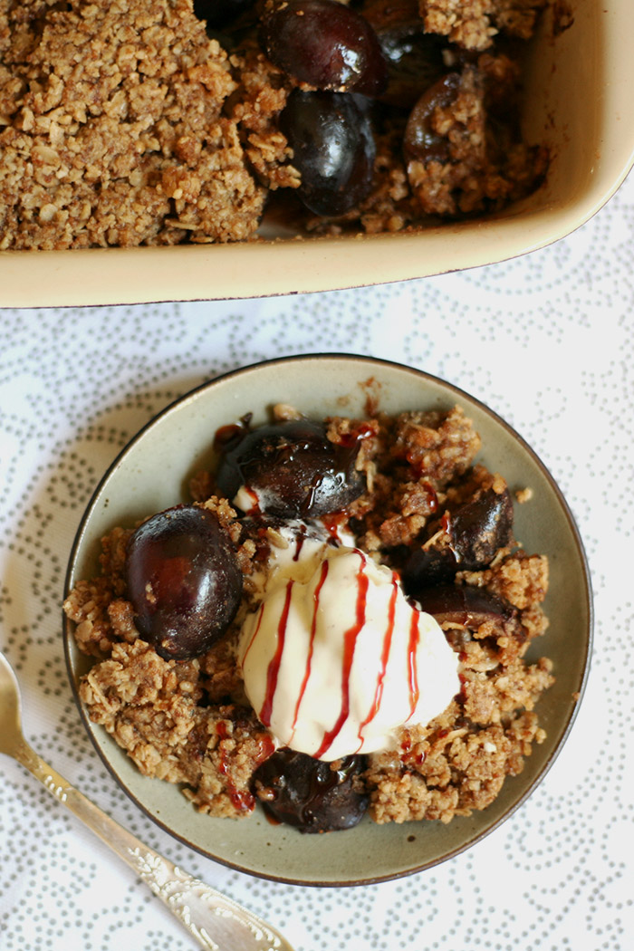 Little green plate with crumbles and plums and a scoop of vanilla ice cream from above