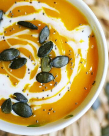 Simple Pumpkin Cream Soup from fresh Hokkaido pumpkin - Pumpkin soup in a small bowl sprinkled with pumpkin seeds, chia seeds and dairy-free cream poured on top.