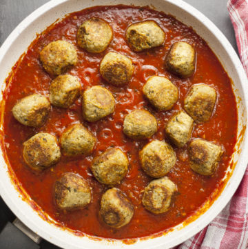 Overlay photo of a frying pan. Lot of small eggplant balls in marinara sauce