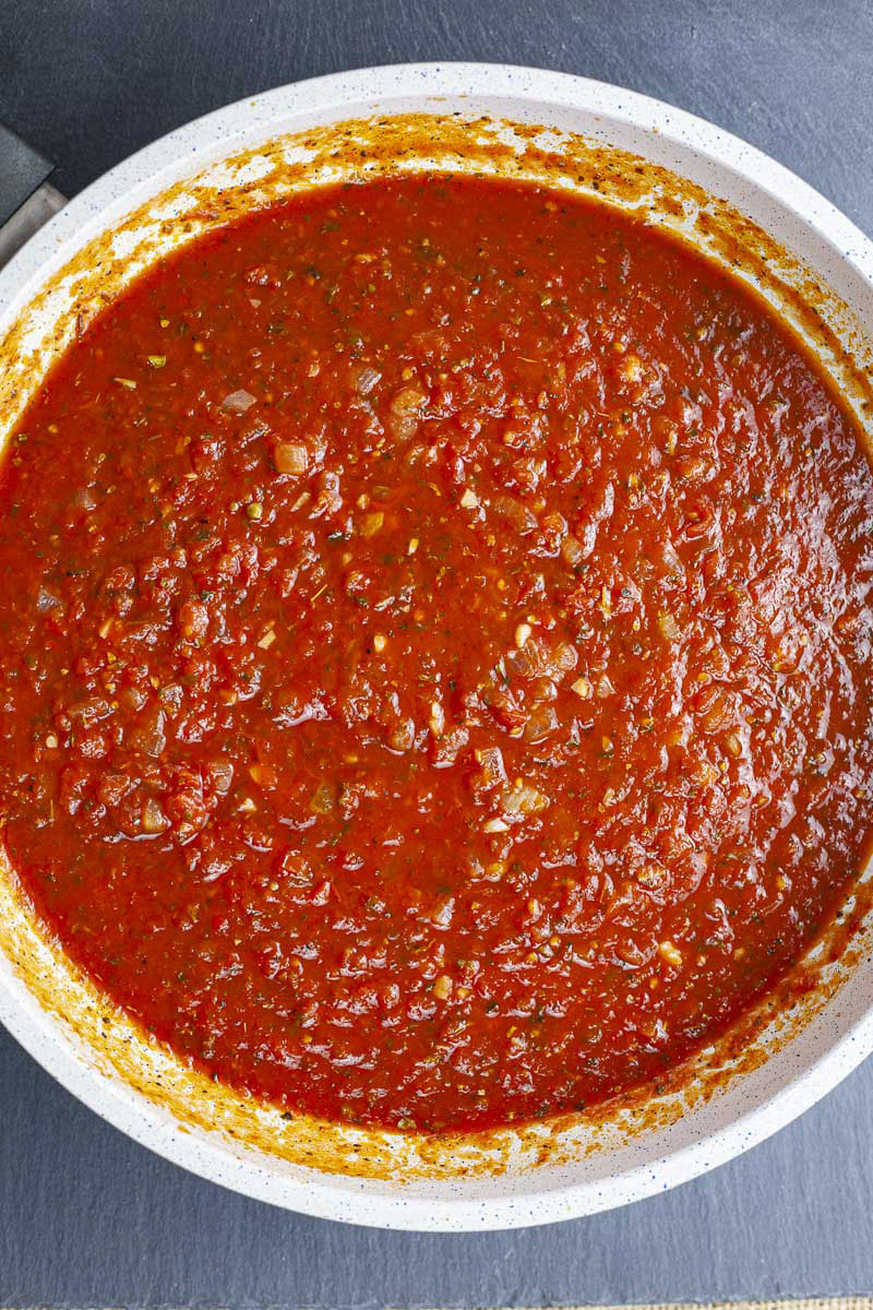 A large saucepan from above with lots of chunky red sauce with yellow and green bits and pieces ready to be served on pasta.