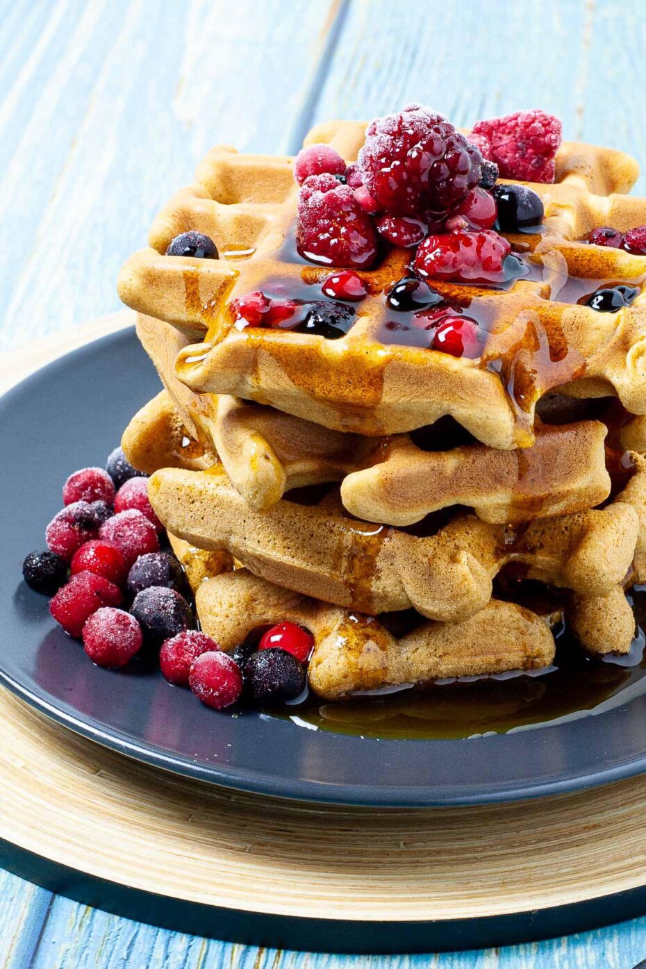 Black plate with a stack of waffles topped with mixed berries and maple syrup
