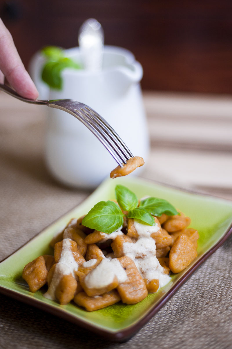 Orange rectangle pasta with white sauce on a green plate topped with fresh green basil leaves. A fork is lifting one up in the air.