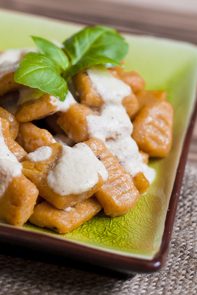 Orange rectangle pasta with white sauce on a green plate topped with fresh green basil leaves