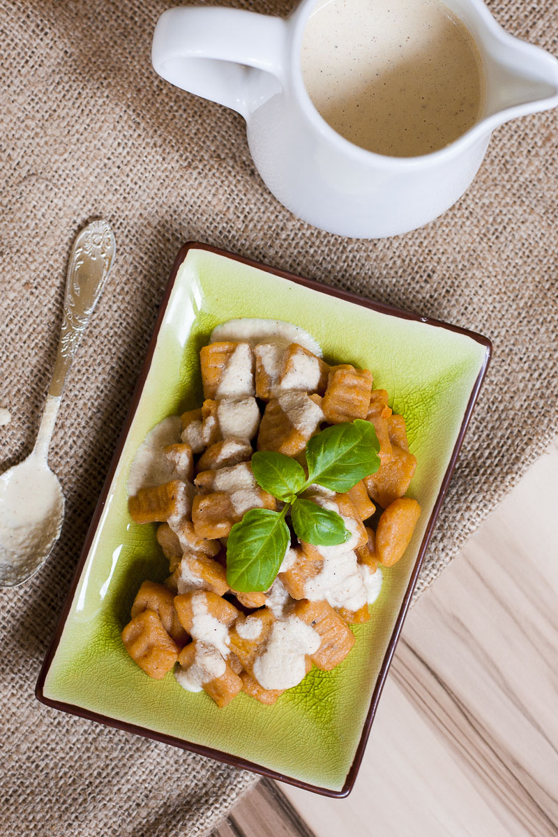 From above orange rectangle pasta with white sauce on a green plate topped with fresh green basil leaves. 