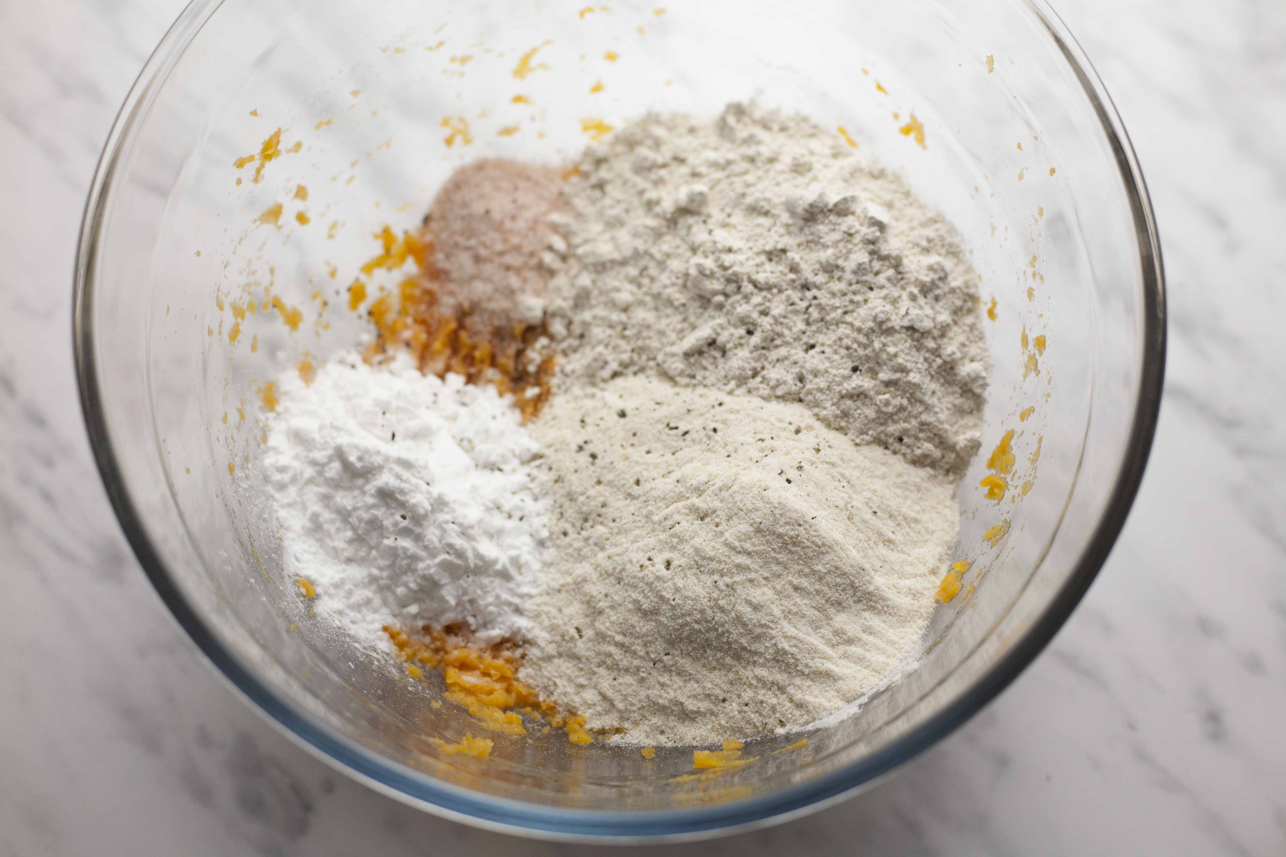 Glass bowl with mashed orange puree and heaps of flours and powders. 