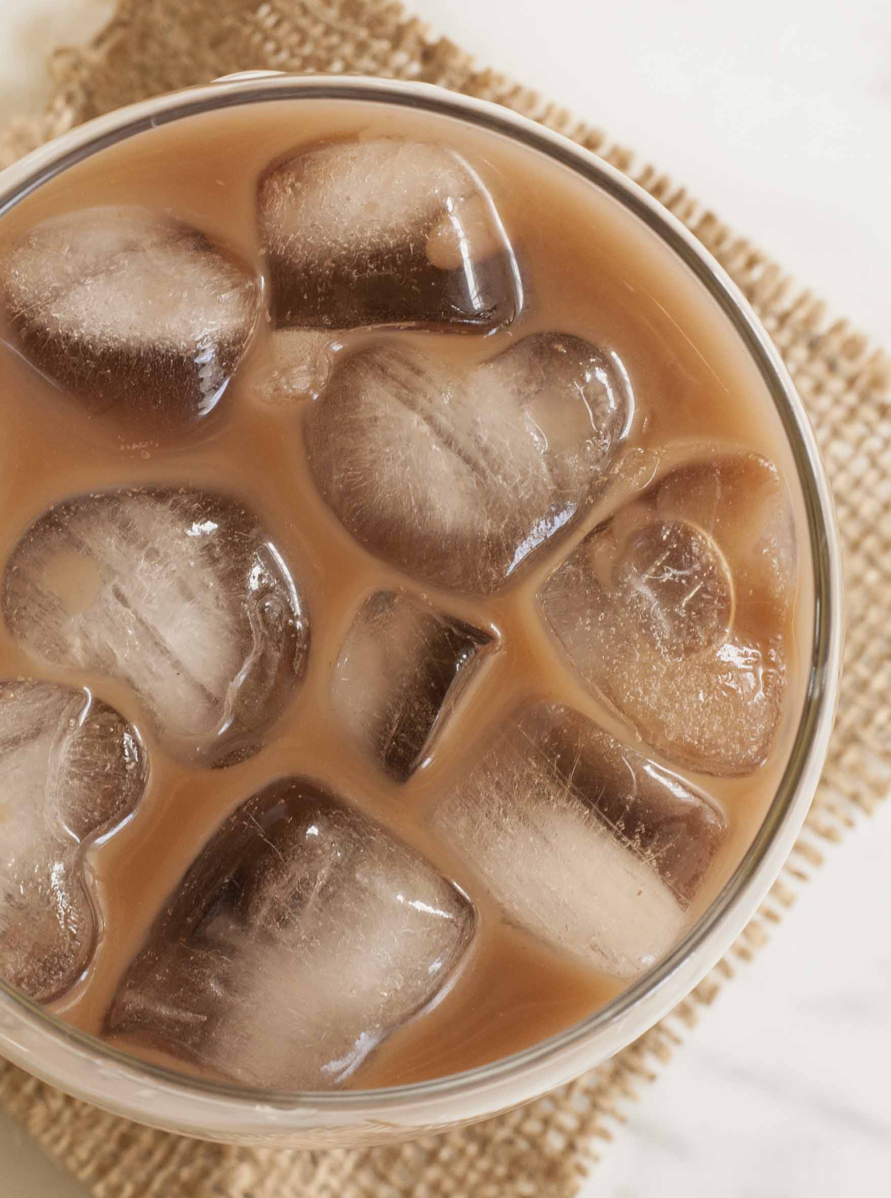 A whiskey glass with brown creamy drink and heart-shaped ice. 