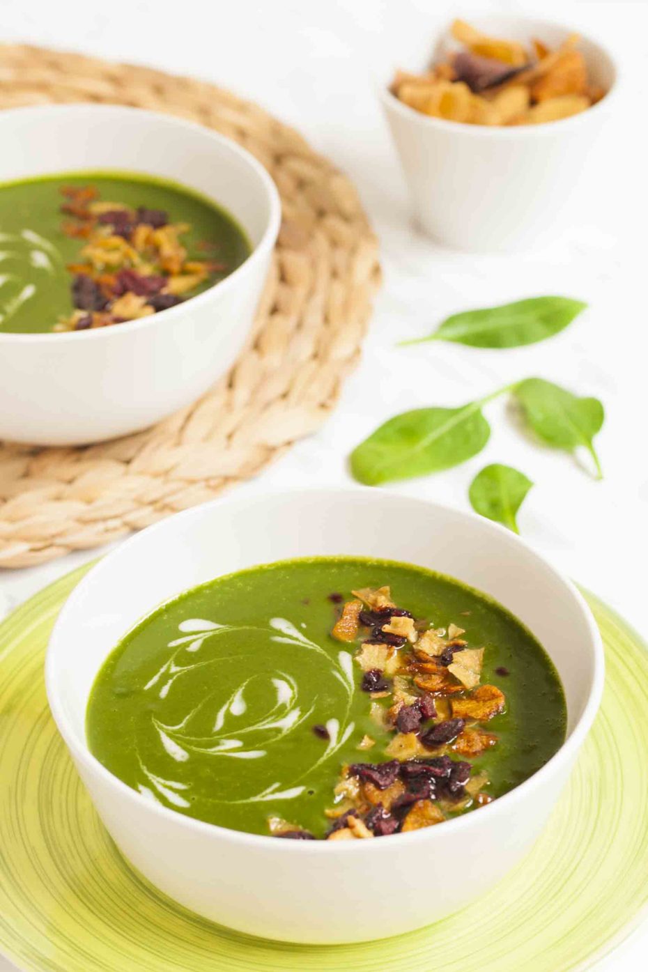 2 bowls of vegan spinach soup sprinkled with vegetable crisps and dairy-free cream swirls.