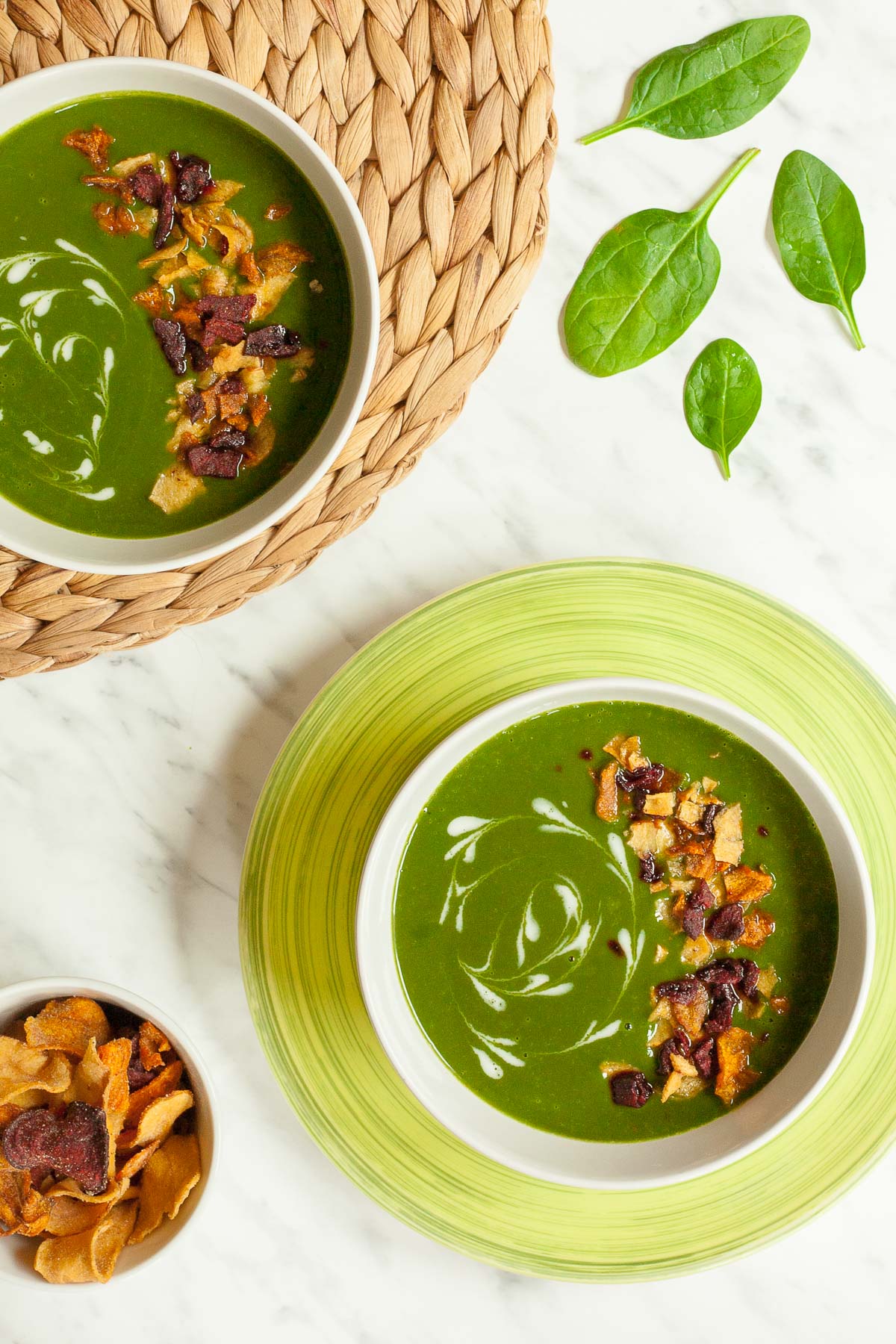 2 bowls of green soup sprinkled with vegetable crisps and white swirls.