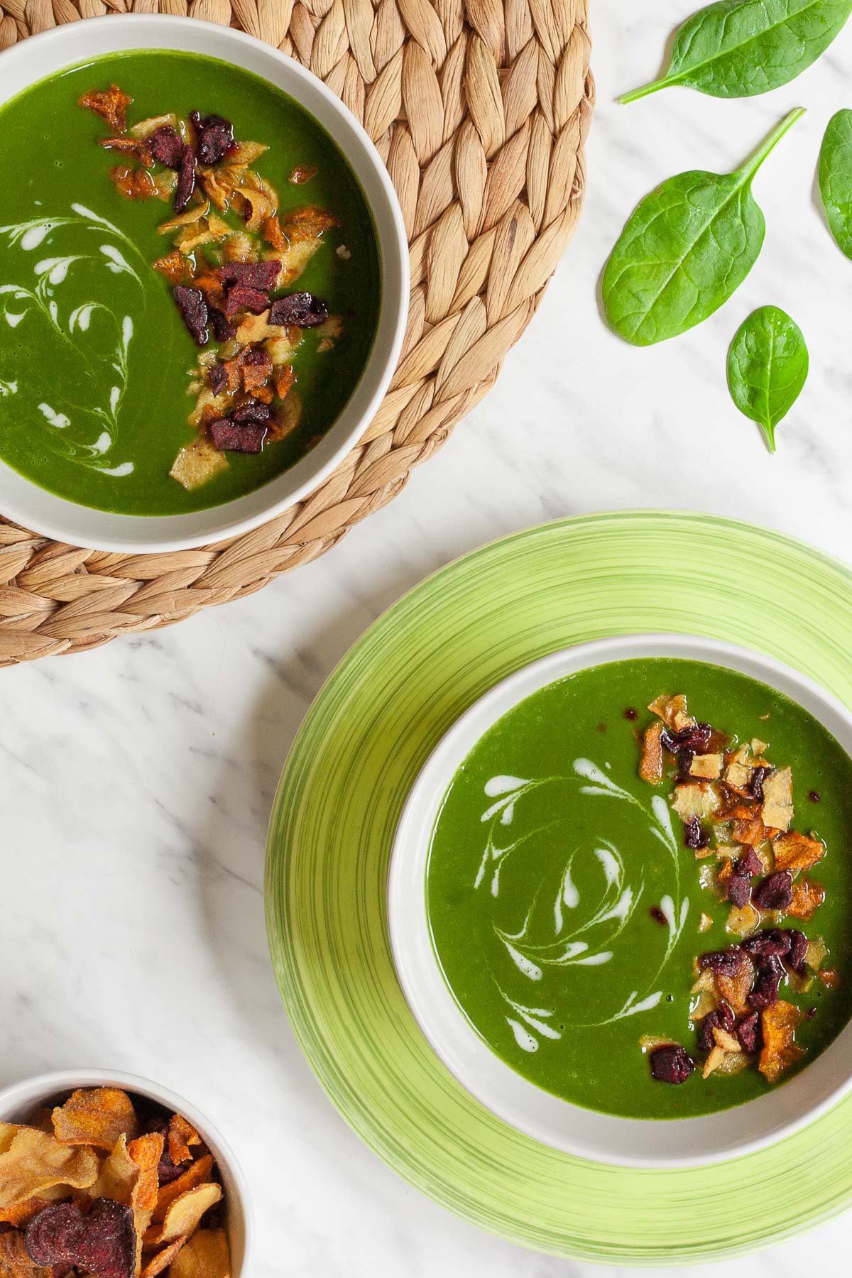 2 bowls of green soup sprinkled with vegetable crisps and white swirls.