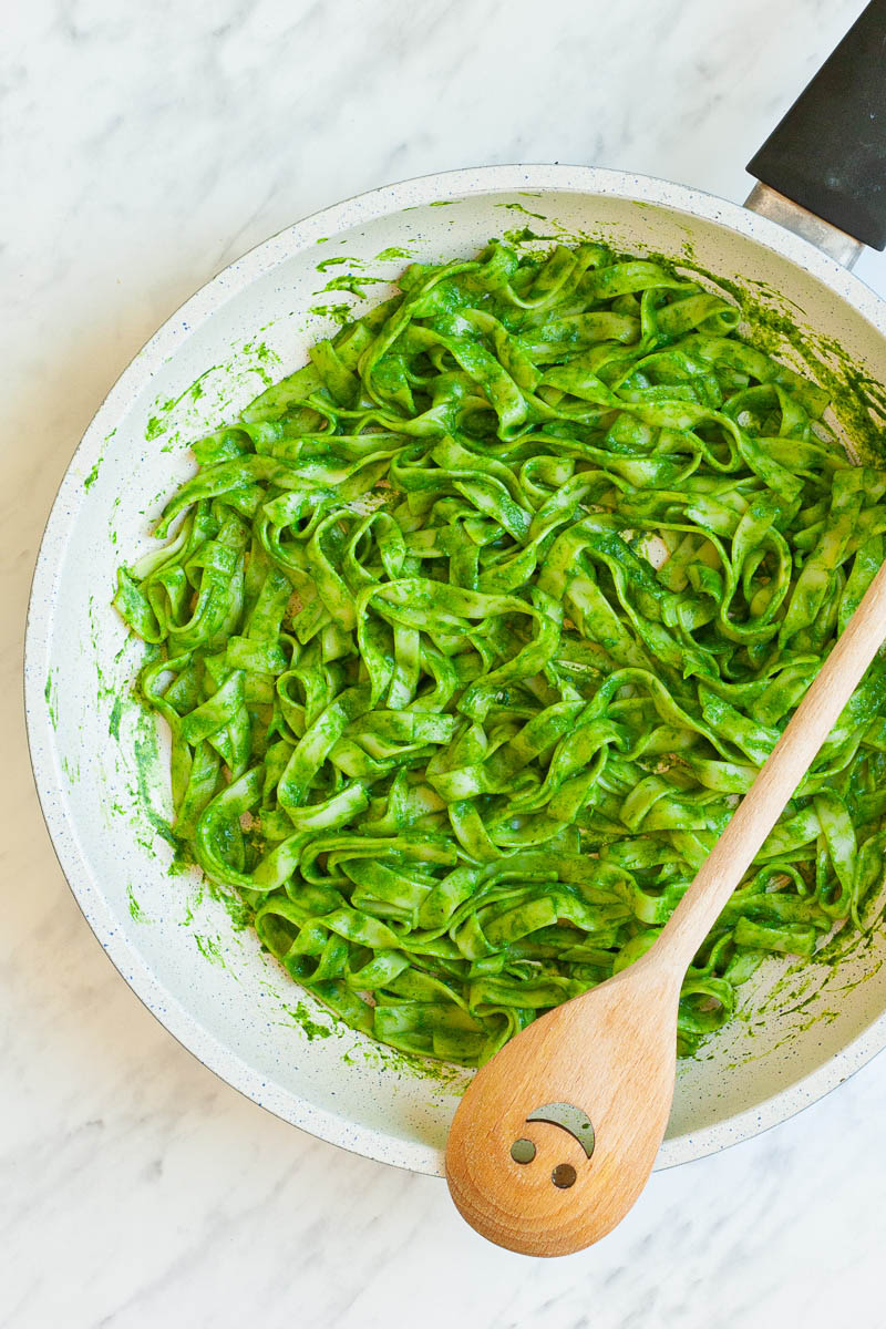 A white frying pan from above with fettuccine pasta covered in green sauce