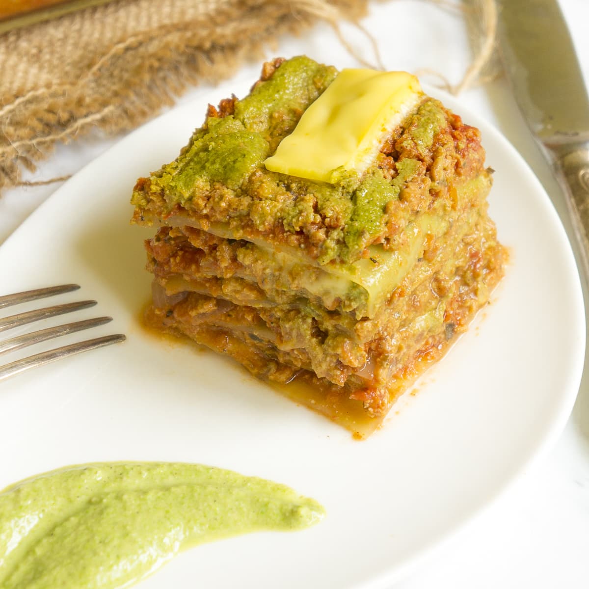 A slice of vegan cabbage lasagna on a white leaf-shaped plate with a smear of spinach alfredo on the side