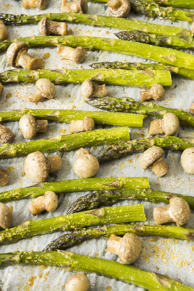 Close-up of roasted asparagus spears and small champion mushrooms on parchment paper