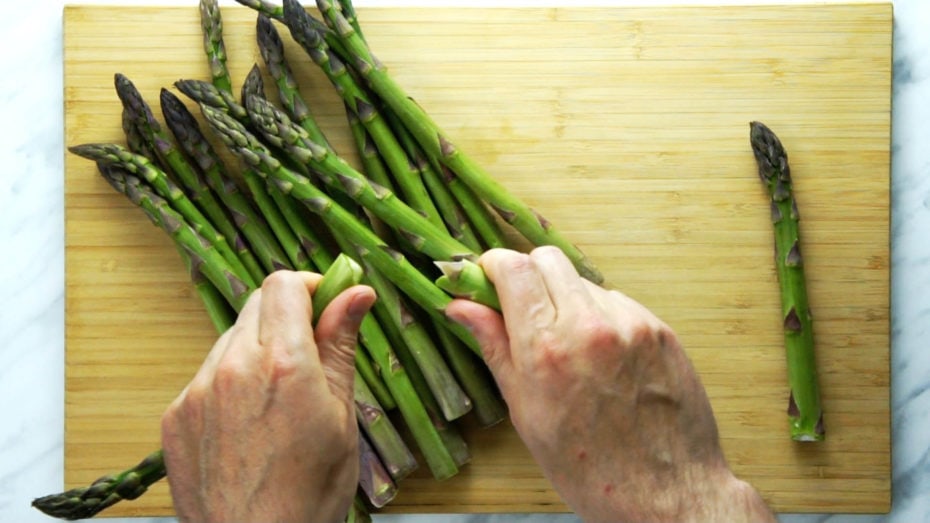 Close-up of how to snap asparagus stalk with hands above a wooden board full of fresh asparagus