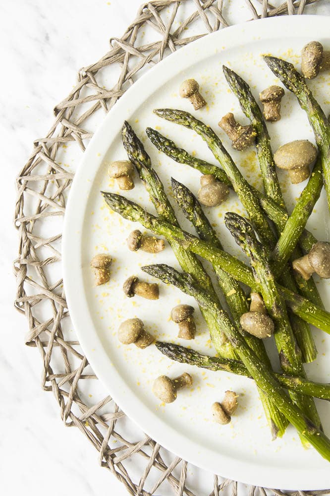 White plate with roasted asparagus and mushrooms styled as messy sprinkled with extra seasoning