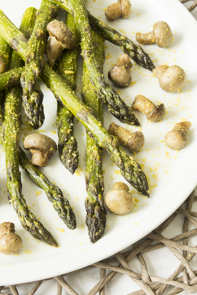 White plate with roasted asparagus and mushrooms styled as messy sprinkled with extra seasoning