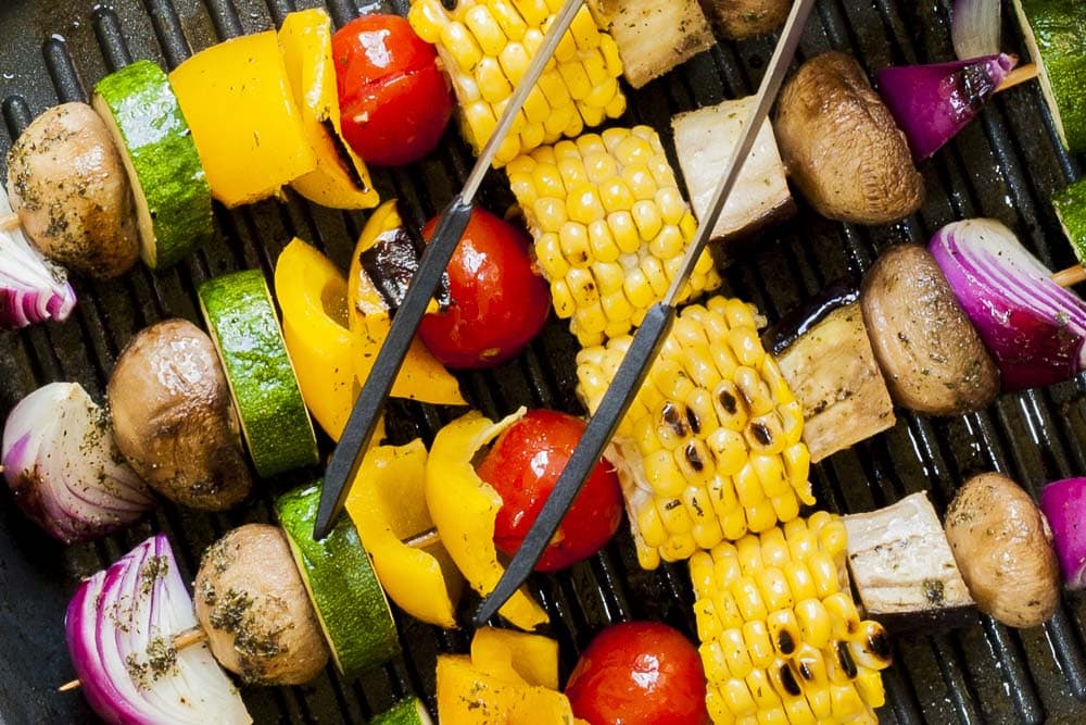 Close-up of the grilled vegetable kabobs in a grill pan with tongs