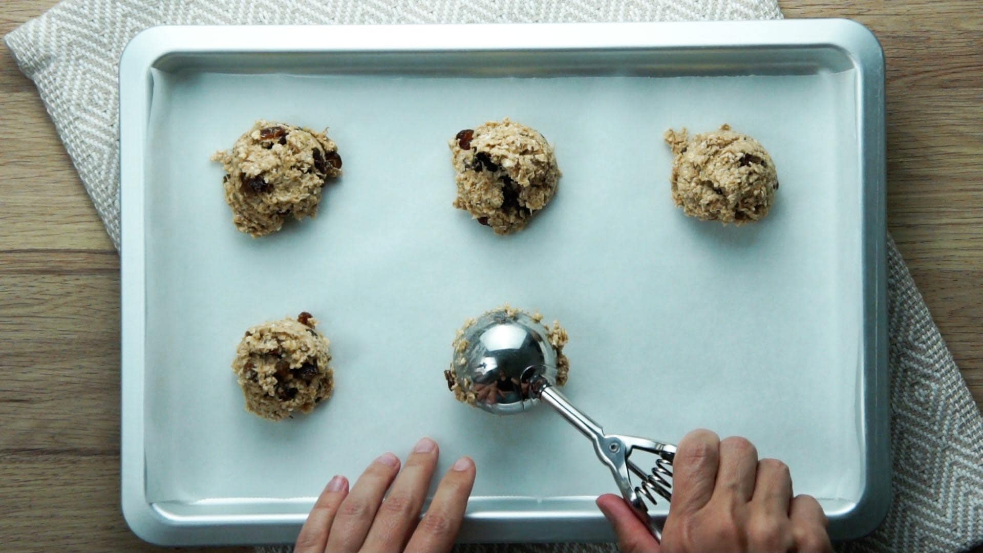 Sheet pan with a parchment paper and 3-ingredient cookie dough is placed on it with the help of an ice cream scooper