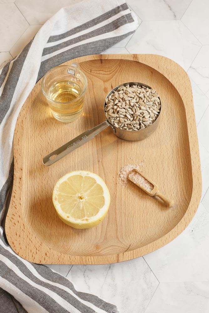 Ingredients of dairy-free sour cream - On a wooden board there are a cup of sunflower seed, half of lemon, small glass of apple cider vinegar and a wooden spoon of salt.