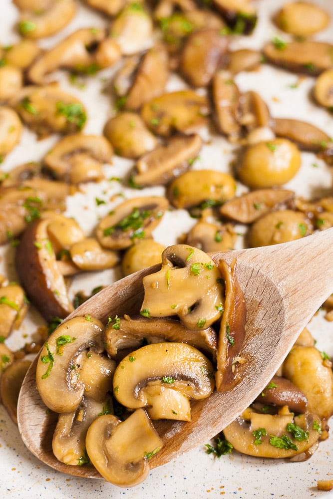 Close-up of a wooden spoon with sauteed mushrooms in soy sauce, garlic and parsley
