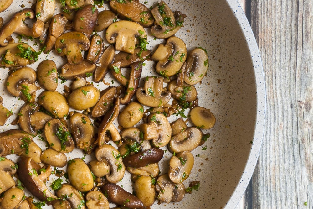 Frying pan full of sauteed mushrooms in soy sauce, garlic and parsley