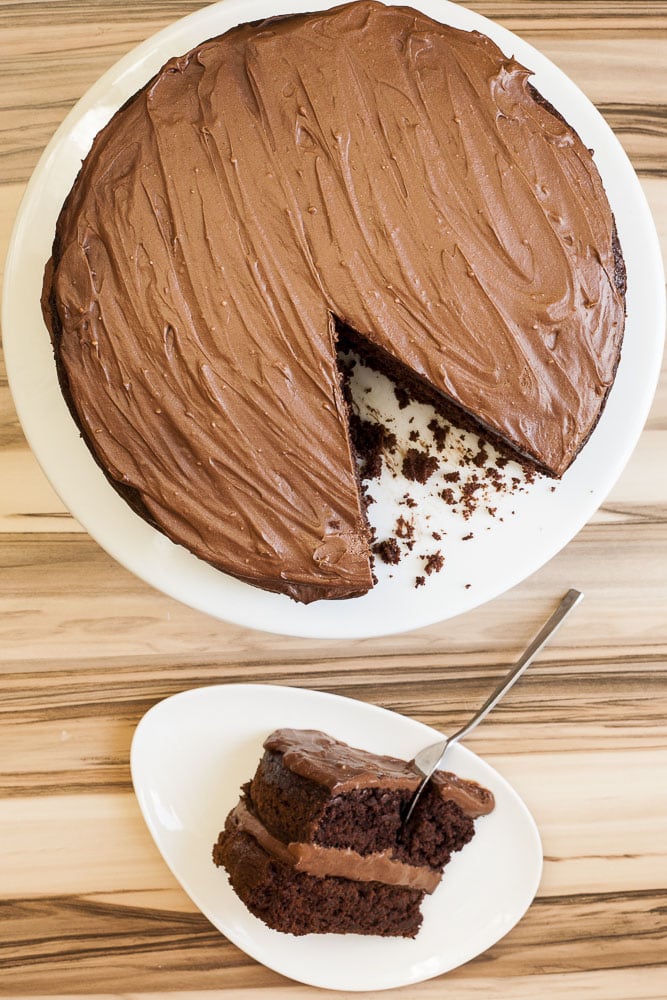 Vegan gluten-free cake from above on a white cake stand. Next to it a slice of cake on a white plate with a fork