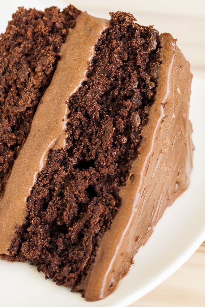 Close-up of a vegan chocolate cake slice with chocolate coconut whipped cream frosting on a white plate
