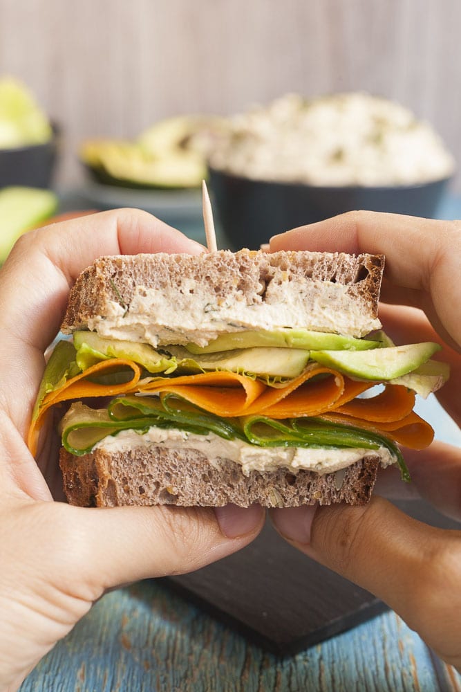 Close-up of a a sandwich with two layers of tofu cream cheese with thinly sliced cucumber, carrot, lettuce and avocado slices