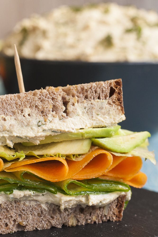 Close-up of a a sandwich with two layers of tofu cream cheese with thinly sliced cucumber, carrot, lettuce and avocado slices