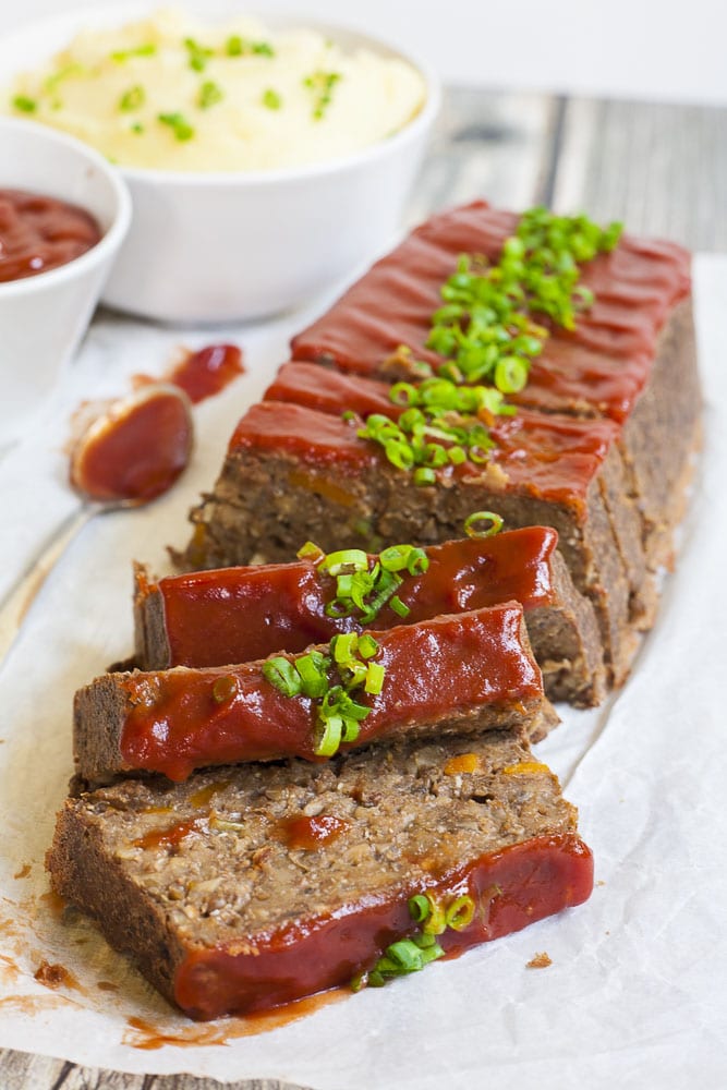 Vegan lentil loaf on parchment paper from above with maple tomato glaze and chopped spring onion. 