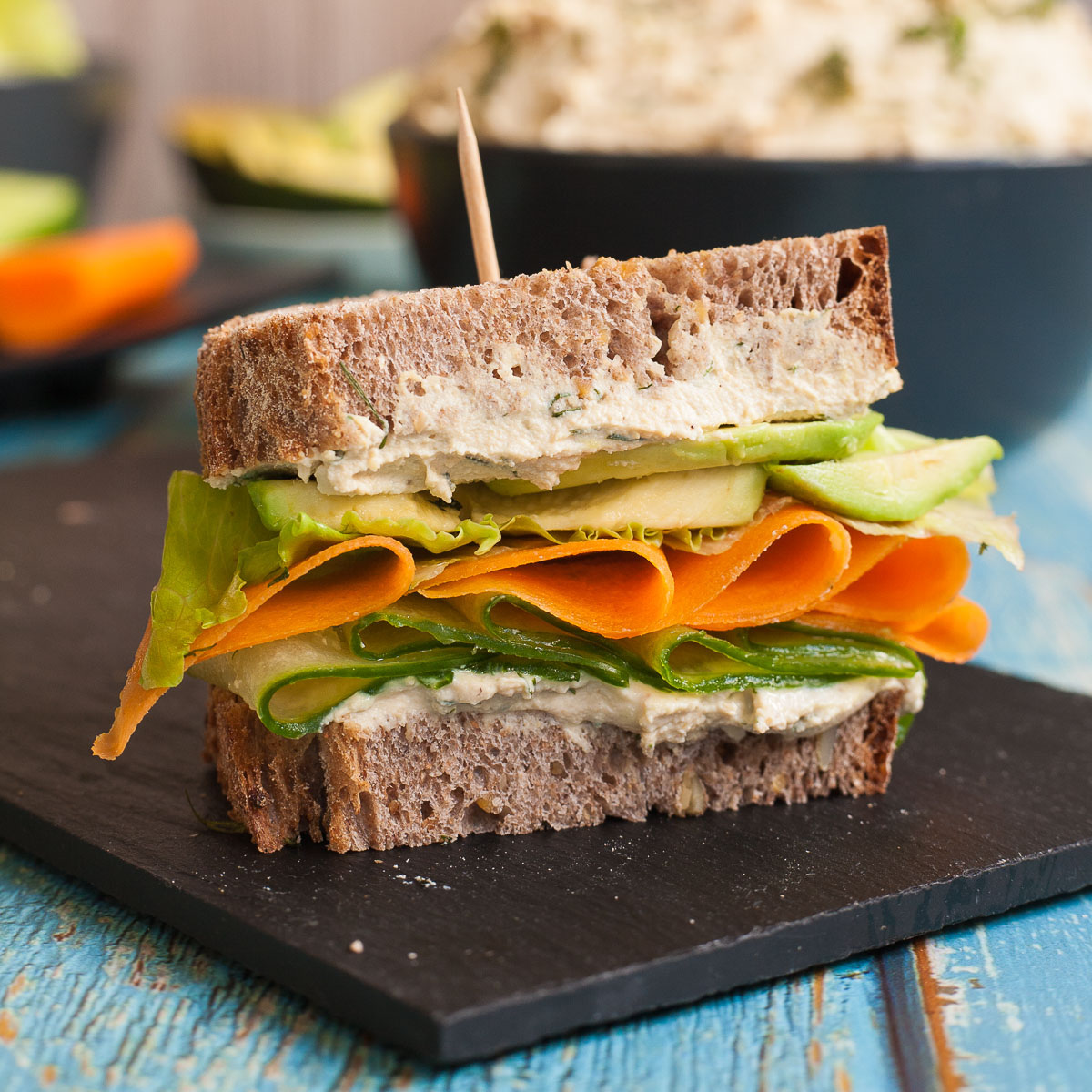 Close-up of a a sandwich with two layers of tofu cream cheese with thinly sliced cucumber, carrot, lettuce and avocado slices