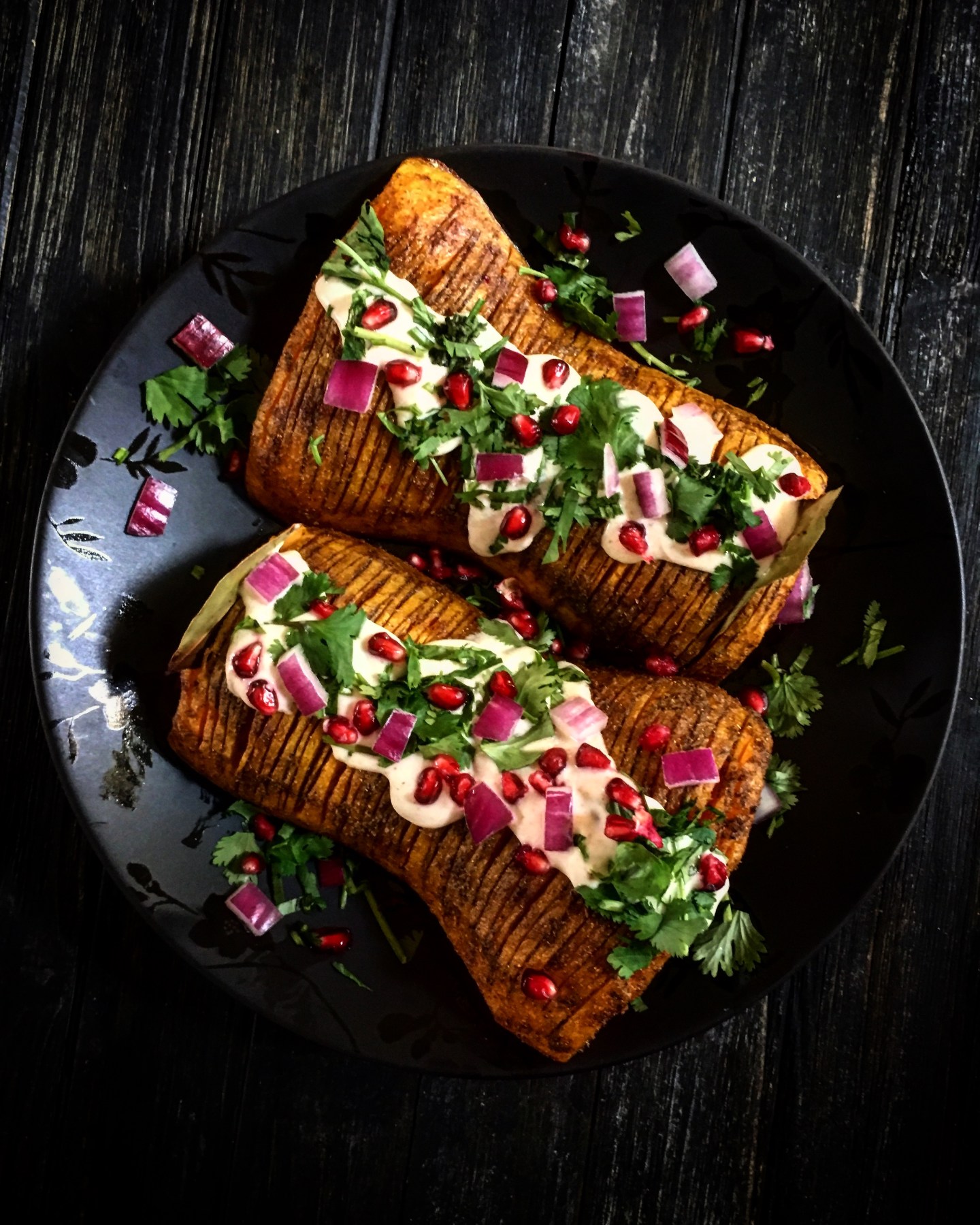 2 halves of a butternut squash is thinly incised and baked. They are topped with a white sauce, chopped purple onion, pomegranate seeds and parsley. 