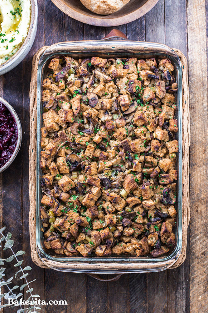 A rectangle-shaped glass pan from above is full of charred bread cubes, mushroom slices and chopped green herbs. 