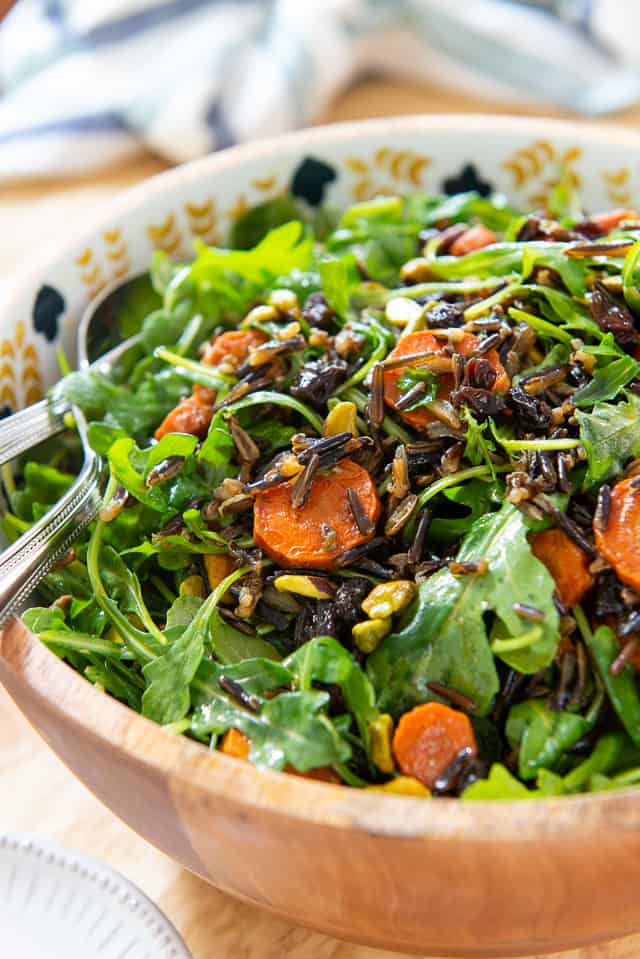 Wooden salad bowl with arugula, sliced carrots, black rice and pistachios