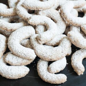 A large stack of crescent cookies on a black plate. Dusted with sugar.