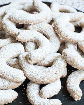 A large stack of crescent cookies on a black plate. Dusted with sugar.