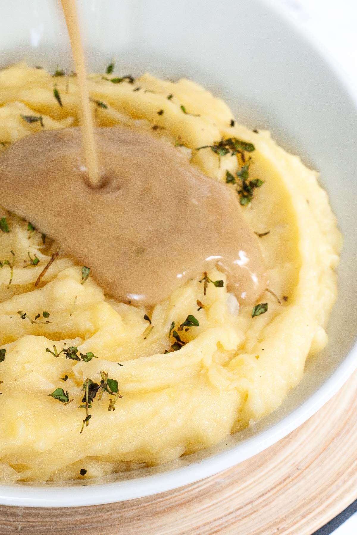 White bowl with mashed potatoes. Light brown gravy is pouring on top of it.
