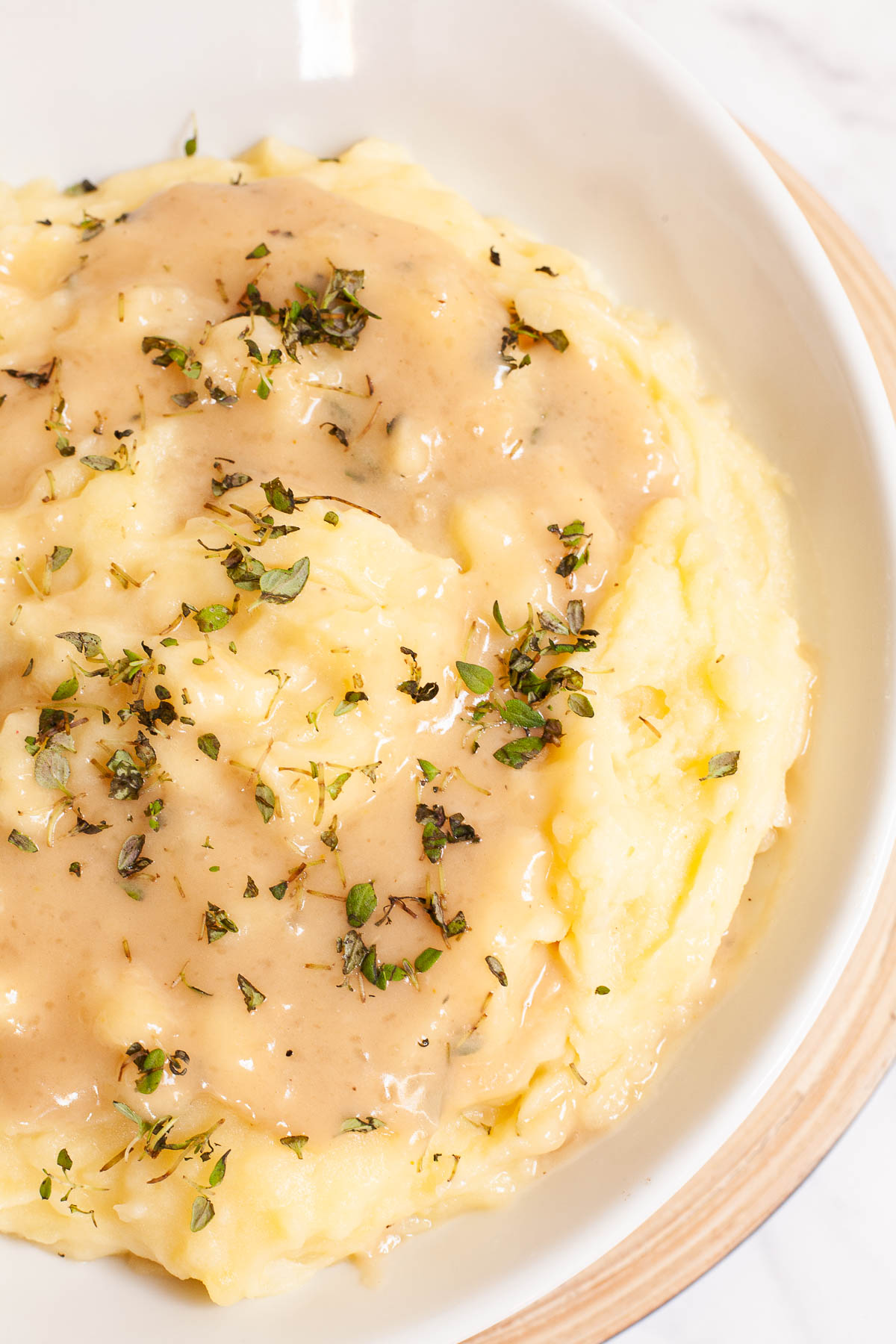 White bowl with mashed potatoes, with light brown gravy and chopped herbs.
