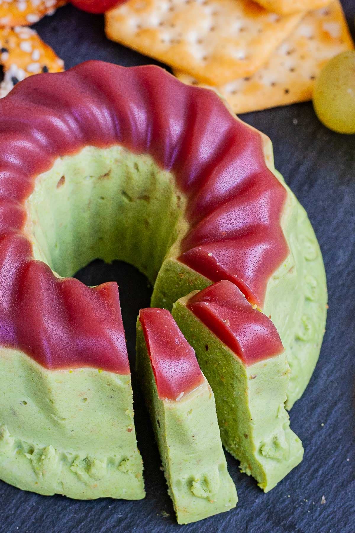 Green cheese shaped as a bundt topped with dark pink jelly. Two slices are slightly ajar. 