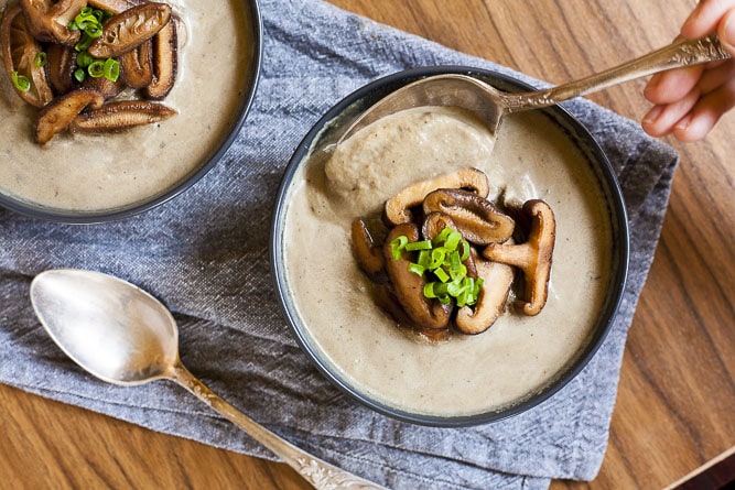Taking a spoonful of the Vegan Cream of Mushroom Soup that is topped with sauteed shiitake mushrooms and spring onion