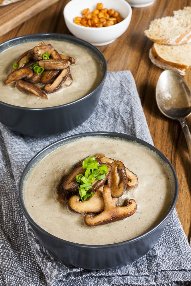 Vegan Cream of Mushroom Soup in two black bowls topped with sauteed shiitake mushrooms and spring onion