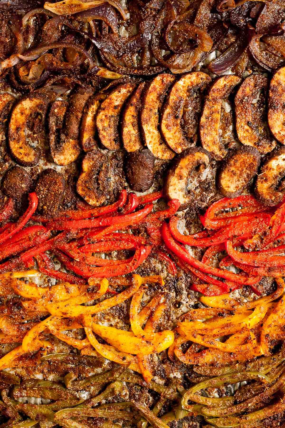 Close-up of roasted brown crispy seasoned red, yellow, green bell pepper strips and mushroom slices after baking.