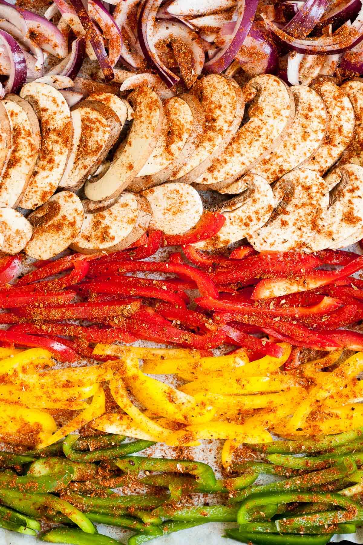 Red yellow green bell pepper and mushroom slices in a sheet pan seasoned with different spices before baking