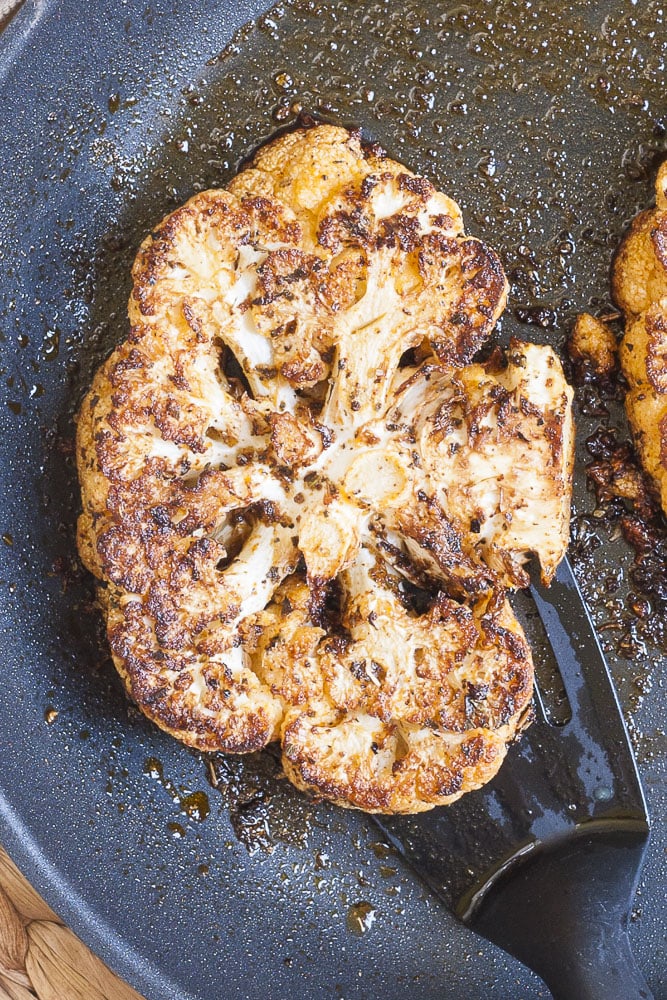 A brown crusted cauliflower steak in a frying pan with a slotted turner.
