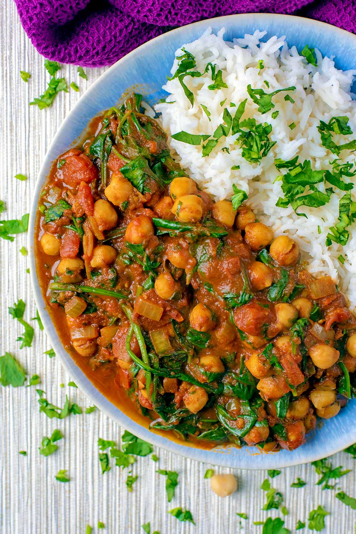 Blue bowl with rice sprinkled with green herbs and chickpeas and wilted spinach in a red-brown curry sauce