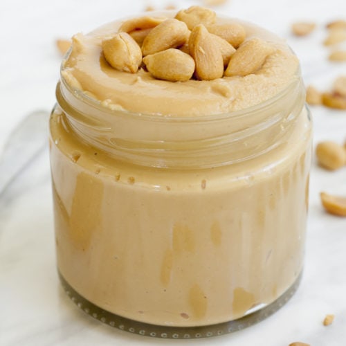 A small jar with light peanut butter topped with chopped peanuts.