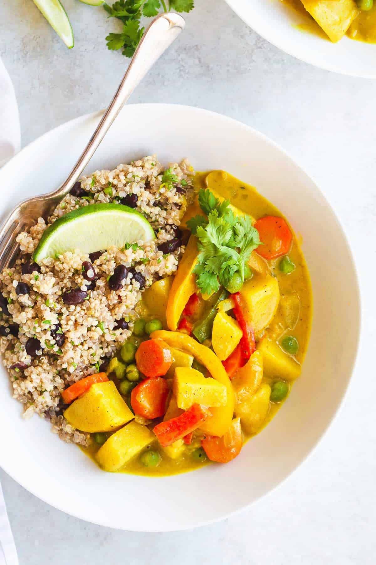 White bowl with quinoa, black beans, and a vibrant yellow mixed veggie curry.